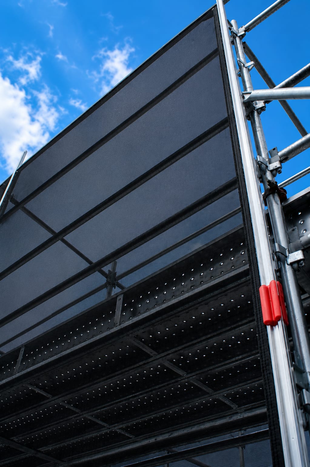 Mesh containment panel installed on a construction scaffold, viewed from below against the sky